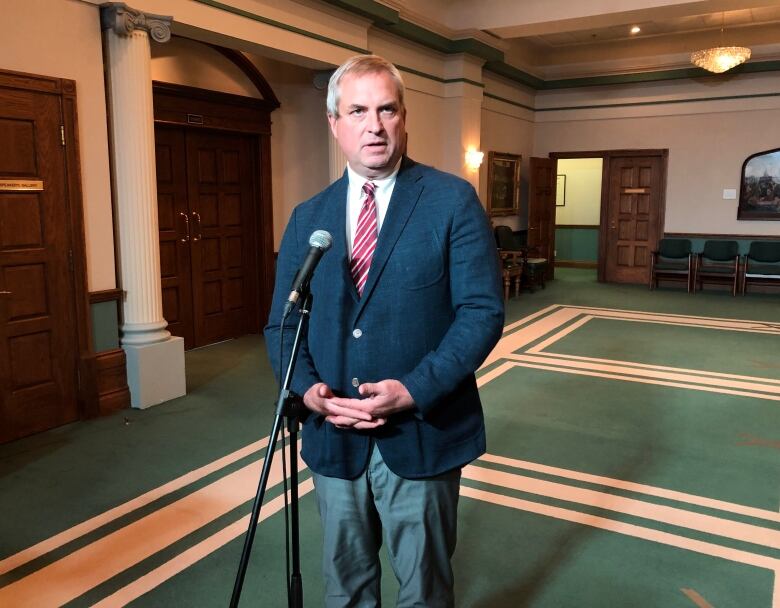 A knees-up shot of a person in a navy suit speaking into a microphone.