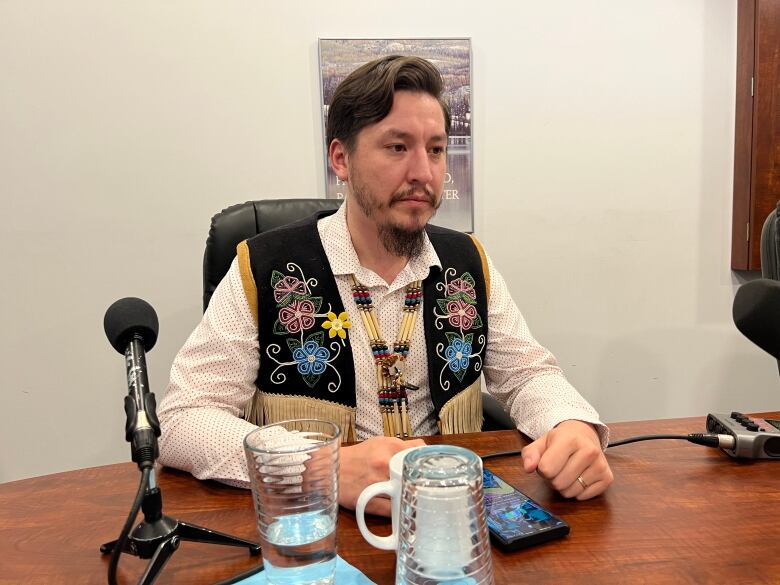 A man sits at a table behind a microphone.