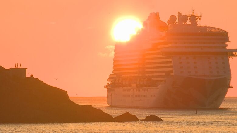 A large cruise ship next to rocky cliffs at sunrise. 