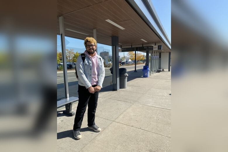 A young student is standing on the platform of a bus terminal and smiling.