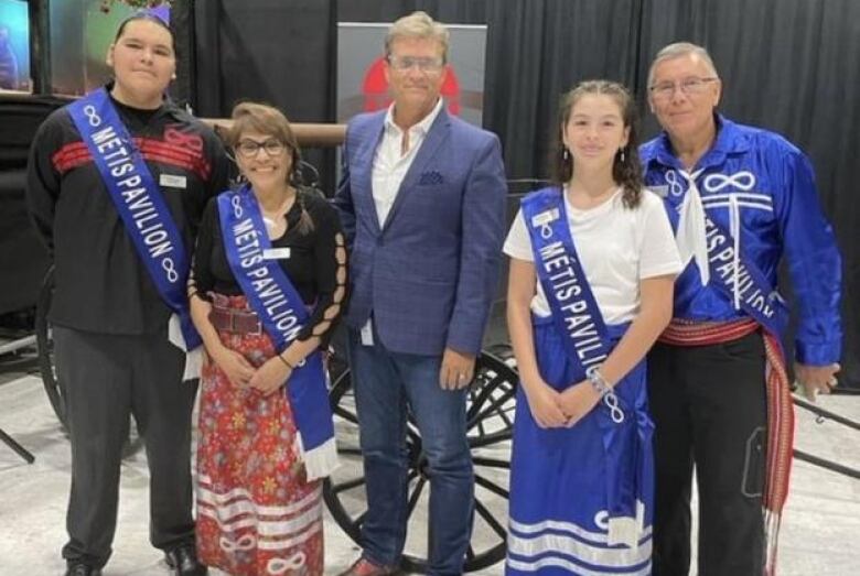 A person in a suit stands in a group of people wearing sashes that say 