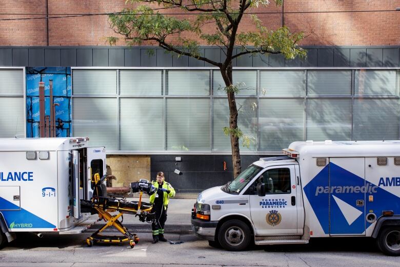 A paramedic stands beside an ambulance outside a hospital