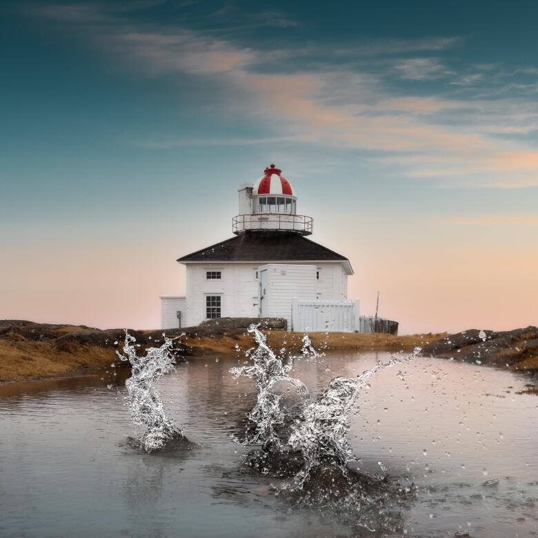 The lighthouse at Cape Spear at sunrise, a small pond in the foreground with splashes of water in the air.