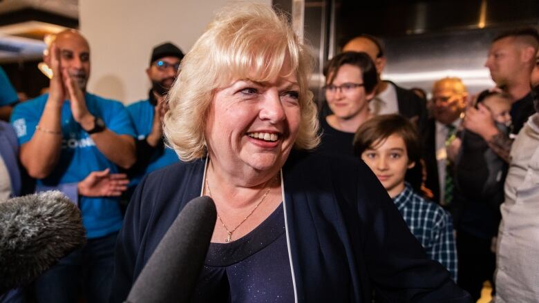 Brenda Locke, a blonde white woman, smiles in a crowded room.