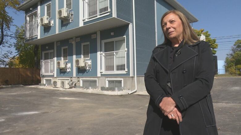 A woman in a black coat in front of a blue house