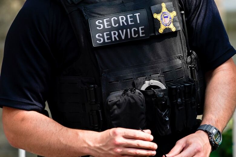 The torso of a security officer is seen with a Secret Service badge visible. 