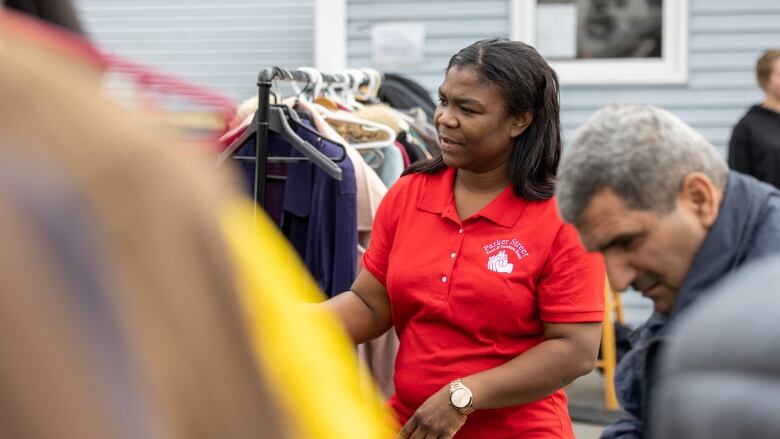 a woman wears a red shirt stands near a rack of clothing.