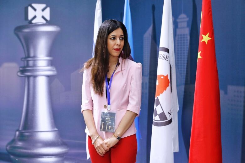 A woman with long dark hair stands beside a staue of a cess piece and red flags with yellow stars. 