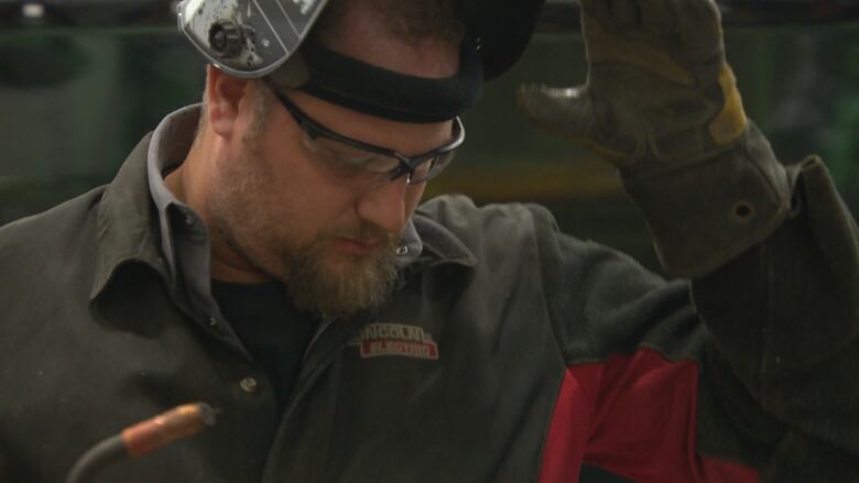 A man looks down as he lifts up a welding mask.