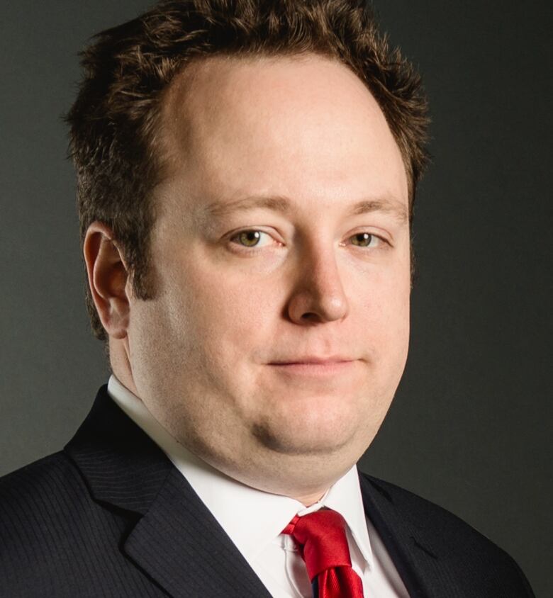 A portrait of a solemn man in a black suit with a red tie.