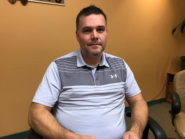 A portrait of a sitting man in a grey polo shirt with a faint smile on his face.