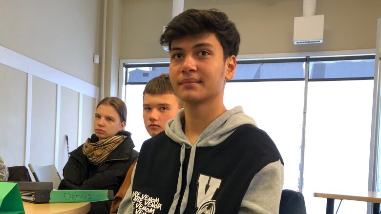 A young man, centre, sits in a classroom with several other students.