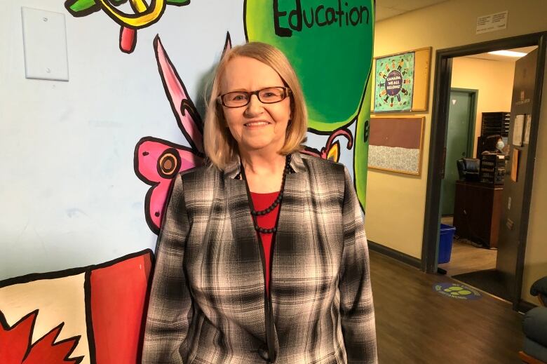 A smiling woman stands in front of a wall painted with a Canadian flag and a green circle with the word 