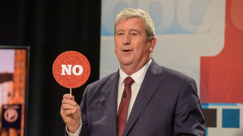 A man wearing a suit is holding up a red sign with the word 