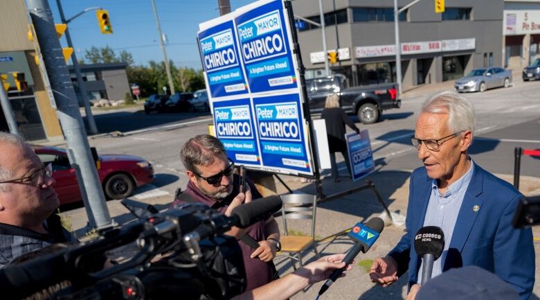 Peter Chirico speaks to reporters standing on a street corner in downtown North Bay, with his election signs behind him.