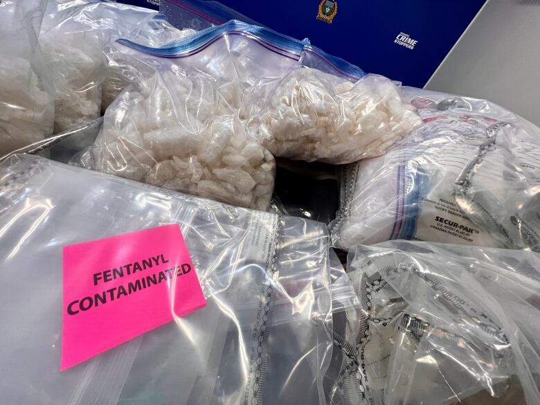 Several plastic bags filled with drugs are seen on a table. One bag has a label with the words 