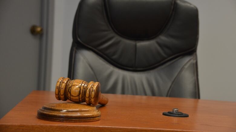 A gavel sits on a council table in front of a large, black chair