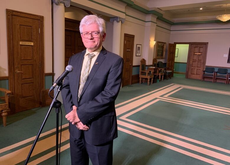 A person in a suit stands at a microphone.