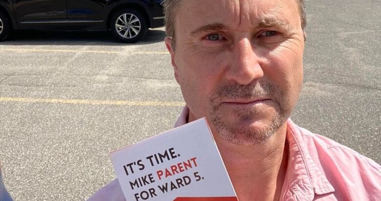 Mike Parent frowns while standing in a parking lot, holding one of his own election pamphlets. 