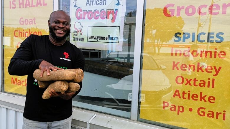 A man holds an armful of large yams, easily a foot long each.