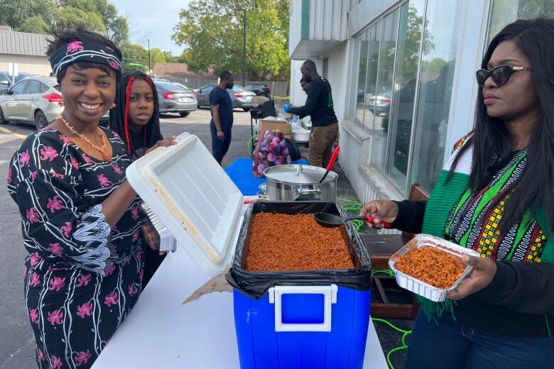 Three women stand around a blue cooler full to the brim with bright red rice. They spoon it out into takeaway containers.