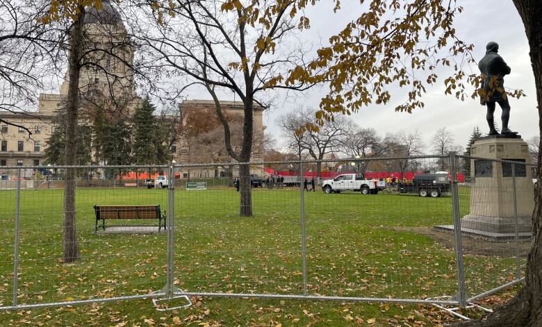 A temporary wire fence surrounds an area of green space in front of a large domed building.