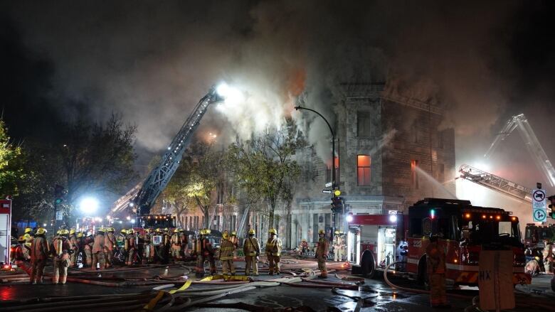 Dozens of firefighters standoutside a greystone building at night. 