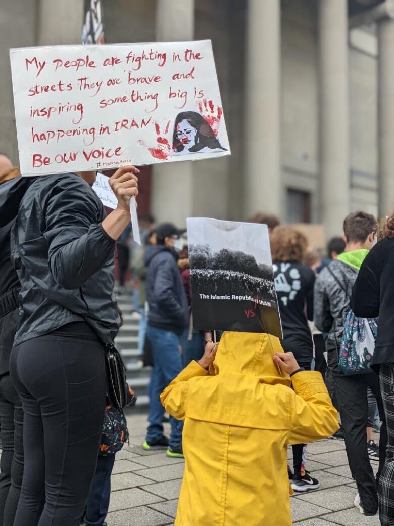 Two people hold signs at a rally. One reads: my people are fighting in the streets. They are brave and inspiring. Something big is happening in Iran. Be our voice.