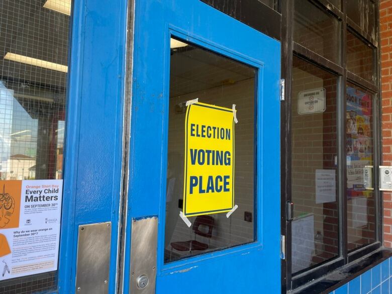 A blue and yellow sign in front of a door reads 