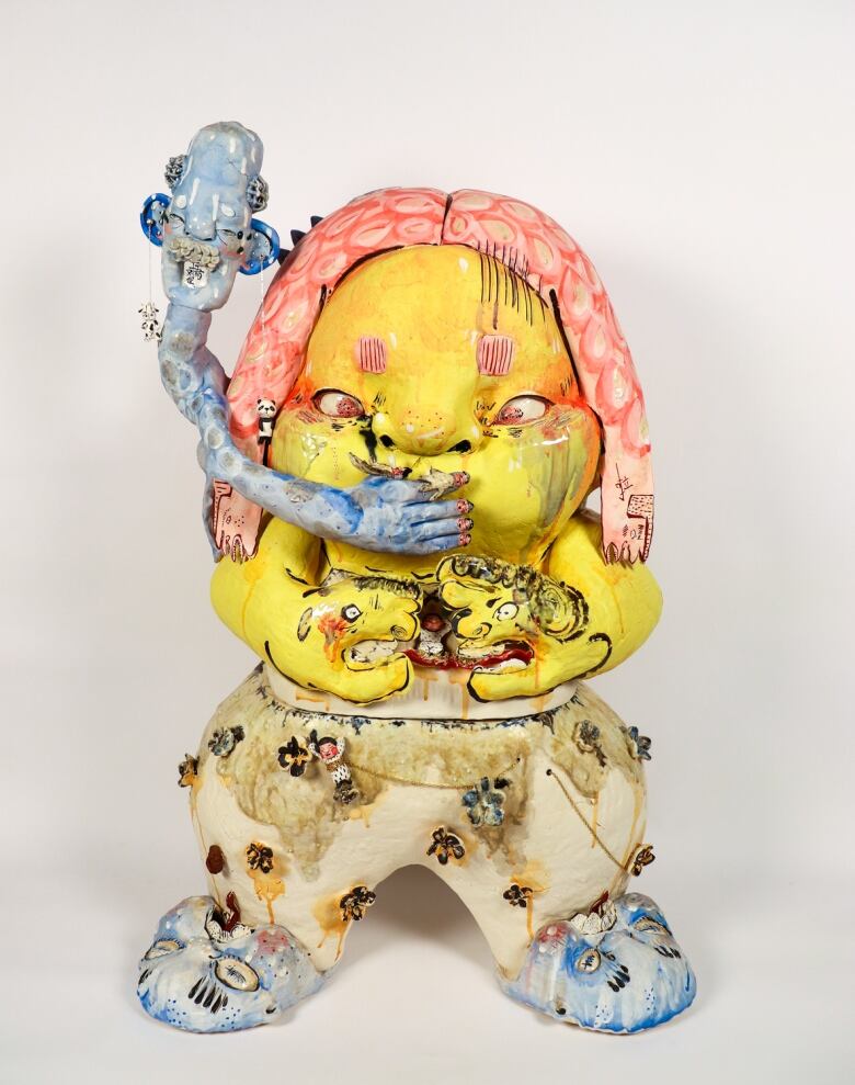 Photo of a ceramic form of a pudgy child painted in yellow, blue and orange.