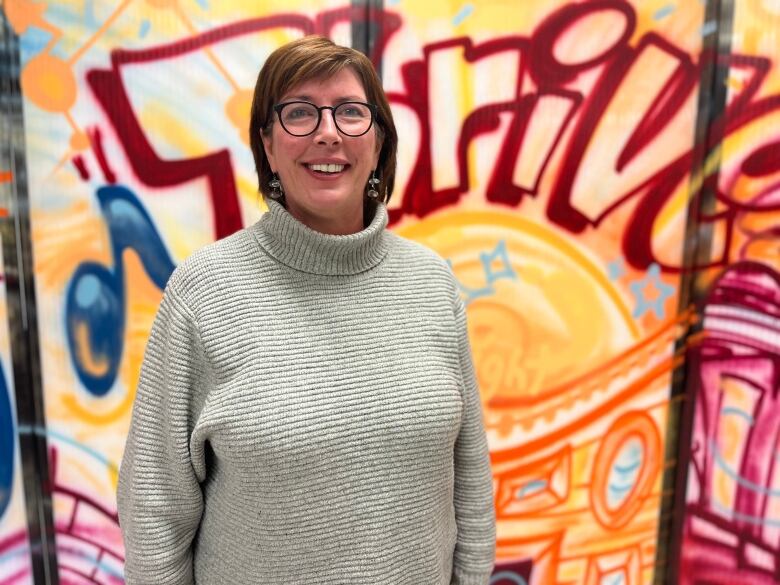 A woman with short hair stands smiling in front of a wall with THRIVE painted in graffiti style lettering. 