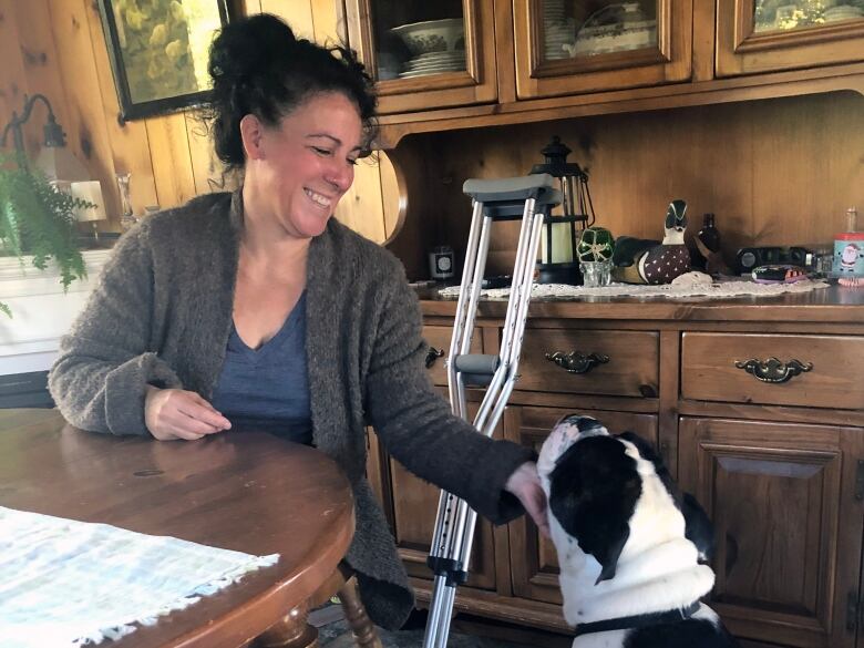 Woman sitting in at a dining table scratches the chin of a black and white dog.