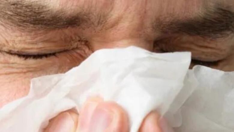 A man furrows his eyebrows while blowing his nose.