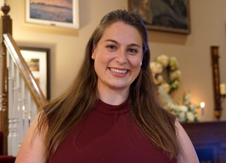 A woman wearing a maroon dress smiles in her home.