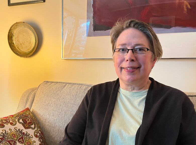 A person smiles into the camera. They sit on a couch.