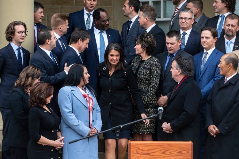 A group of people stand on steps behind a podium and microphone. 