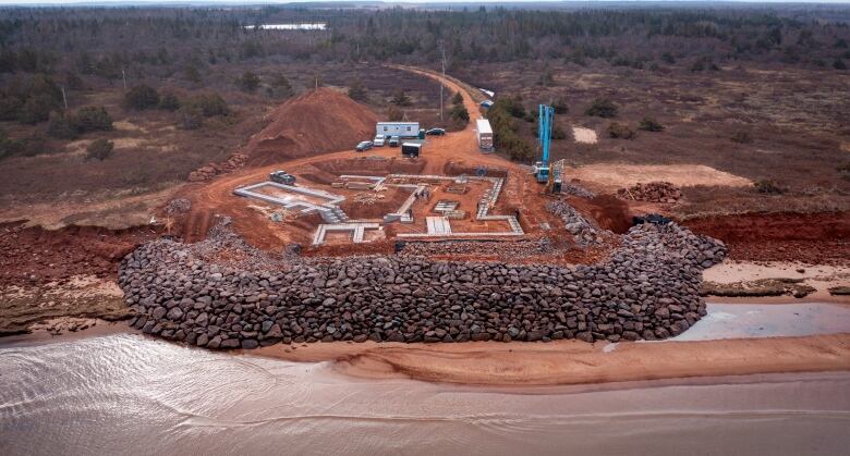 A building with a prominent wall under construction by a shoreline.