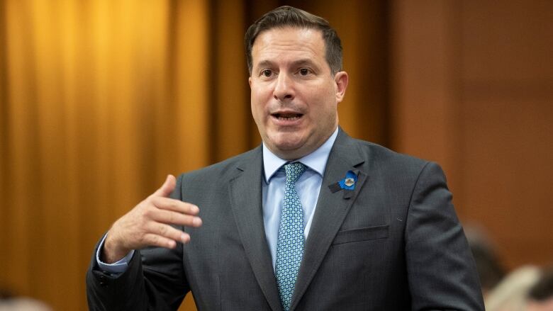 A man in a grey suit with a blue shift and a green tie stands.