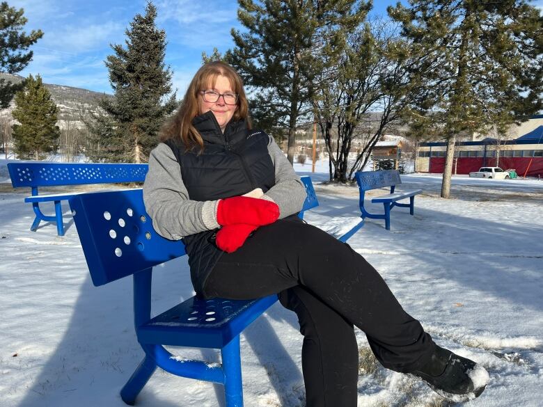 A woman in red mittens sits on a park bench in the snow.