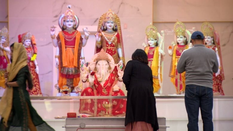 People stand before a colourful Hindu temple with Ganesha in the front, a Hindu god that is an elephant-headed man.