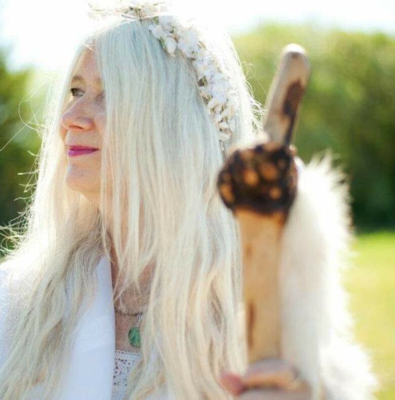 A woman dressed in white holds a wooden staff.