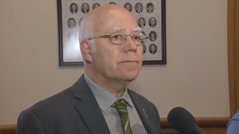 A man in a suit and glasses looks off camera standing in a hallway. 