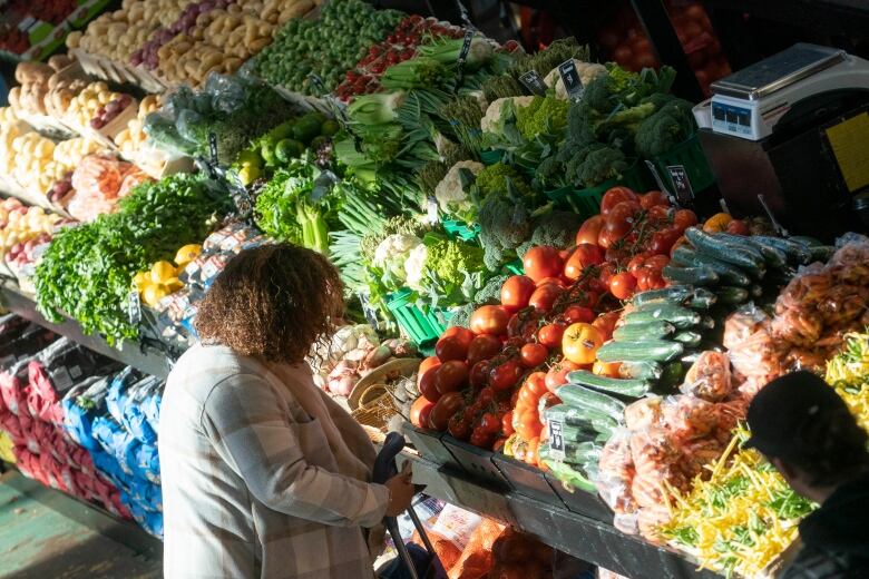 A woman, seen from behind, stands in front of abundant supply of vegetables.