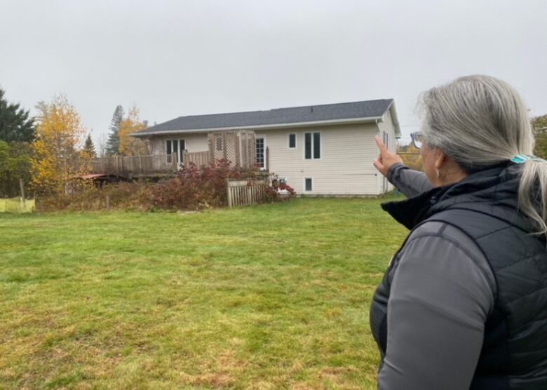 A woman points toward a small, white house.