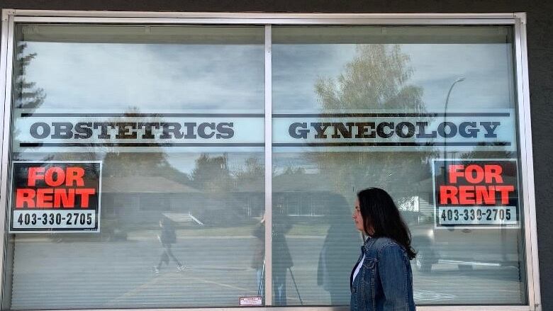 A woman walks in front of the window of an obstetrics clinic. On the window there are two 'for rent' signs