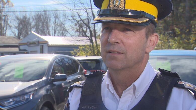 Man in RCMP uniform stands in front of cars.