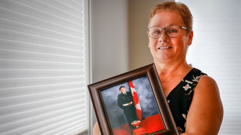 A woman stands next to a window holding a framed photograph.