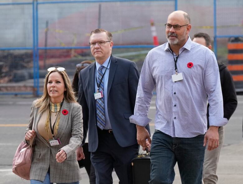 Three people with lanyards walk on a sidewalk.