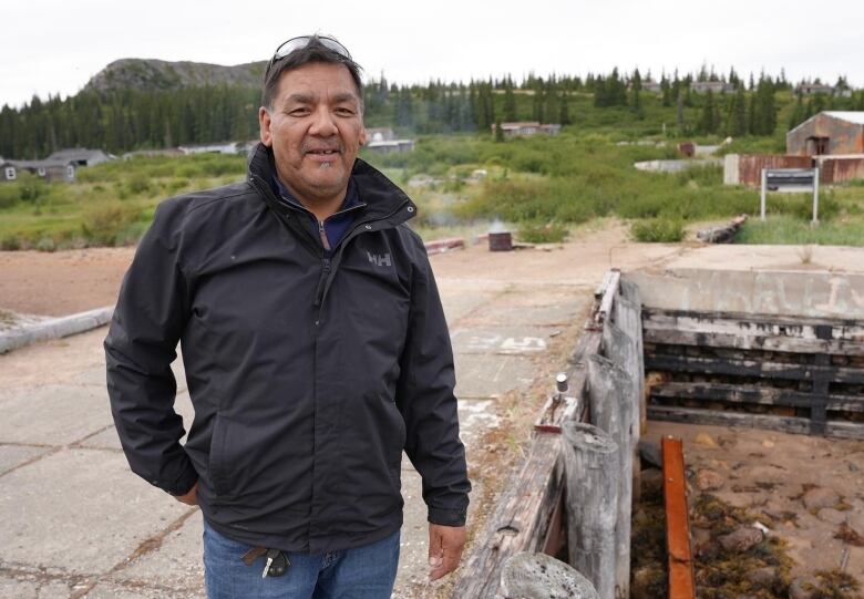 A man stands in front of mountains looking at the camera. 