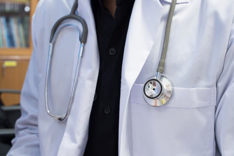 A closeup shows a stethoscope hanging around the neck of a person wearing a white lab coat.